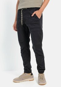 Sort joggerbukser med elastiske manchetter, snøre i taljen og sidelommer. Lavet af en blanding af bomuldsstof med en glat overflade.