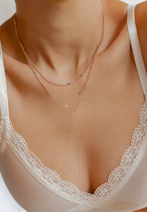 Collana delicata a strati con sottili catene d'argento, caratterizzata da un design a forma di Y e piccole perline decorative, adagiata su uno sfondo di tessuto chiaro.