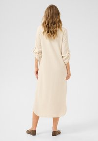 Beige linneklänning med trekvartsärmar, rundad nederkant och uppkullade ärmdetaljer. Bärs med bruna snörlösa skor.