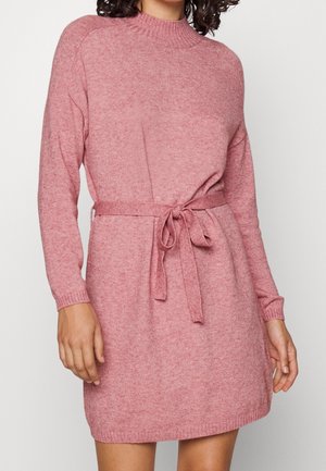 Gebreid roze jurk met lange mouwen, hoge geribbelde kraag, ceintuur in de taille en zijsplitten voor bewegingsgemak. Zachte textuur en casual silhouet.