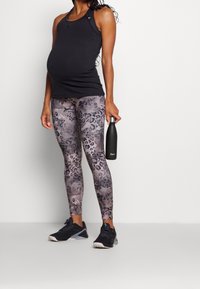Top a canotta nera a coste, leggings grigi con stampa leopardata e scarpe da ginnastica nere. Tienendo in mano una bottiglia d'acqua in acciaio inox nera.