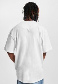 White, short-sleeve t-shirt with a relaxed fit, round neckline, and soft fabric; displayed from the back, worn with blue jeans.