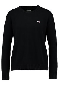 Pull en maille noire à manches longues, avec poignets et ourlet côtelés. Présente un petit logo rouge et blanc sur le côté gauche de la poitrine. Col rond classique.