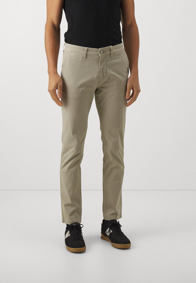 Beige chinos with a slim fit, made of cotton blend fabric. Features a button closure, belt loops, and side pockets. Worn with black sneakers.