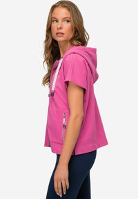 Felpa rosa con cappuccio a maniche corte, dotata di tasca con zip e lacci. Texture morbida con una vestibilità rilassata.