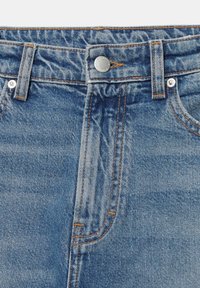 Jean en denim bleu à la taille avec bouton en métal, passants de ceinture et couture orange visible sur tissu délavé.