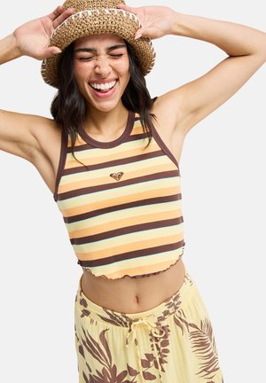 Pasekowany, prążkowany krótki top w kolorach żółtym, brązowym i niebieskim; falowany dół. W połączeniu z żółtymi spodniami z brązowymi kwiatowymi wzorami.