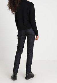 Svart stickad tröja med texturerade axeldetaljer, i kombination med mörkblå tajta jeans och svarta ankelstövlar. Livfulla färger, avslappnad design.