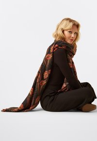 Large black scarf with orange floral design draped over shoulders. Soft texture, fringed edges, and versatile for layering.