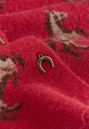 Red wool fabric with a soft texture and a horseshoe-shaped metal accent. The fabric features a light brown and cream pattern.