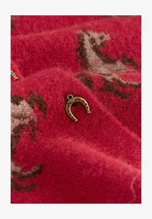 Červená vlnená látka s jemnou textúrou a kovovým akcentom v tvare podkovy. Látka má svetlohnedý a krémový vzor.