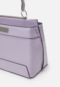 Borsa a tracolla in lavanda con lettering in rilievo "River Island", placca argentata con logo, bordi neri e manico corto attaccato da anelli metallici.