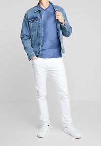 Jeansjacka, blå randig v-ringad skjorta, vita byxor och vita sneakers. Jackan har knappar och bröstfickor. Avslappnad passform.