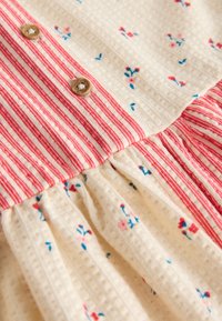 Primer plano de tela crema con pequeños estampados florales rojos y azules, rayas verticales rojas y blancas, y botones de madera.