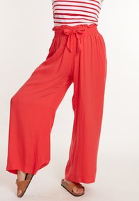 Rode wijde broek met een smocktailleband en een strik. De stof is lichtgewicht en vloeiend, wat het comfort en de bewegingsvrijheid vergroot.