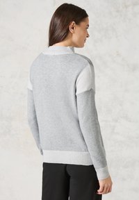 Hellgrauer Pullover mit geripptem Saum und Bündchen. Verfügt über kontrastierende weiße Schulterpatches. Hergestellt aus weichem, strukturiertem Material.