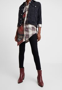 Chaqueta de mezclilla negra superpuesta a una camisa de cuadros con una bufanda estampada, combinada con leggings negros y botines burdeos.