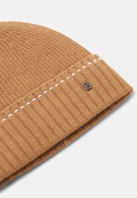 Brązowa dzianinowa czapka z prążkowanym, teksturowanym wzorem. Z kontrastowym białym przeszyciem i małą metalową naszywką z logo.