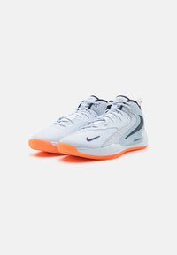 Nike basketball shoes, white with grey accents, feature an orange sole. Textured upper and smooth details enhance design elements.