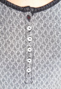 Gray patterned fabric with a textured finish, featuring a round neckline and five white buttons down the front. There’s a red accent button.