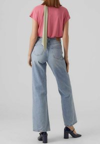 Pink short-sleeve top with a green ribbon detail at the back, paired with high-waisted light blue straight-leg jeans and dark heeled shoes.