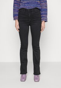 Calças de ganga pretas com um corte justo, bolsos frontais e uma cintura padrão, combinadas com sapatos lilás claros e um suéter de malha multicolorido.