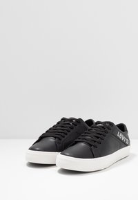 Mustat nahkakengät valkoisella kumipohjalla. Ominaisuuksiin kuuluu mustat nauhat ja näkyvä harmaa logo sivulla. Littee muotoilu ja teksturoitu viimeistely.