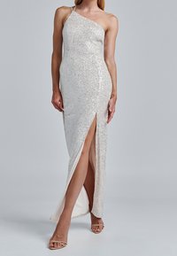Abito lungo monospalla con paillettes argentate, spacco laterale e una fodera interna morbida. Presenta spalline sottili e una silhouette aderente.