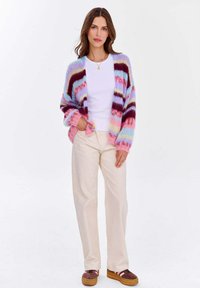 Wielokolorowy sweter z dzianiny z paskami w odcieniach różu, niebieskiego i purpury; luźny fason, długie rękawy. Połączony z białą bluzką i jasnymi spodniami.
