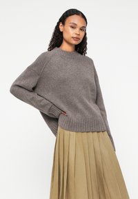 Gray knitted sweater with a ribbed hem, oversized fit, and raglan sleeves, paired with a pleated beige skirt. Smooth texture overall.