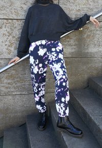 Černý strukturovaný zkrácený svetr s volnými rukávy je sladěn s volnými kalhotami s černobílým květinovým vzorem. Černé šněrovací boty dokreslují celý outfit.