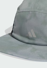 Cappellino verde in tessuto strutturato con design a motivo. Presenta una visiera piatta e un logo grigio a tre strisce sulla parte anteriore.