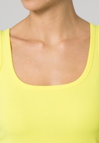 Gul ribbad linne med bred rund halsringning, som visar en jämn textur och en figursydd design som följer kroppens konturer.