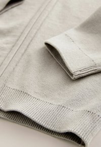 Ljust grått stickat cardigan med en mjuk textur, ribbade ärmslut och en öppen frontdesign med subtila sömdetaljer.