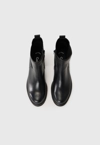 Bottines en cuir noir avec une texture lisse, bout rond et détail de fermeture éclair sur le côté. Elles disposent d'une semelle en caoutchouc plate et basse pour le confort.