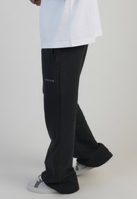 Melnas sporta bikses ar relaksētu piegriezumu, ar sānu kabatām un baltu "SIKSILK" logo. Apvienotas ar baltu T-kreklu un pelēkiem sporta apaviem.