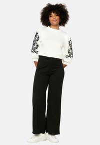 Balta džemperis ar melnu ziedu izšuvumu uz piedurknēm, apvienots ar melnām plašām biksēm un baltām kedām. Gluda tekstūra, ikdienišķs dizains.