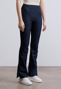 Τζιν με σκουρομπλε χρώμα, καμπάνα και ψηλή μέση, κατασκευασμένα από ντένιμ. Διαθέτουν δύο εμπρόσθιες τσέπες, ομαλή υφή και πλευρικές σχισμές στο τελείωμα.