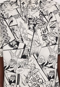 Īsām piedurkņu krekls ar melnbaltu komiksu joslas dizainu, kas satur dažādas paneļus, runas burbuļus un grafiskus attēlus.