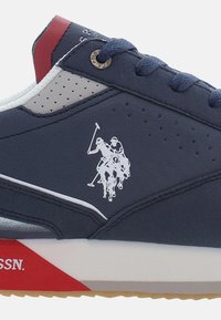 Sneaker in pelle blu con accenti grigi e rossi, dotata di un logo di polo bianco, lati perforati e una suola in gomma testurizzata.