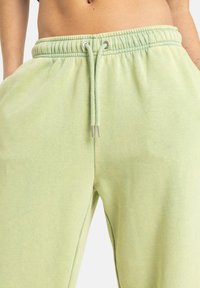 Lysegrønne sweatpants med elastisk talje, snøre og sidelommer; stoffet virker blødt med en let tekstur.