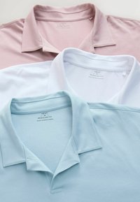 Kolm polo särki, mis on kuhjatud: hele roosa, valge ja helesinine. Igal särgil on klassikaline krae ja sildid taga.