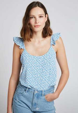 Débardeur bleu clair à motif floral, avec des bretelles volantes et un décolleté rond, associé à un short en denim taille haute.