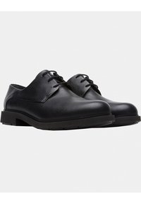 Chaussures en cuir noir avec une texture lisse, bout rond, design à lacets et semelle en caoutchouc épaisse et basse. Style minimaliste sans accents visibles.