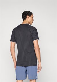 Maglietta atletica nera con sottili righe verticali, maniche corte e scollo rotondo. Indossata con pantaloncini azzurri chiari, che mostrano un tessuto strutturato.