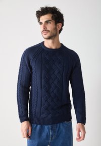 Dunkelblauer Strickpullover mit Kabelstrickmustern, rundem Ausschnitt und gerippten Bündchen. Weiche Textur mit einer leicht taillierten Silhouette.