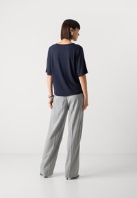 Top corto in navy a maniche corte con una vestibilità rilassata, abbinato a pantaloni ampi grigio chiaro a righe sottili, con una leggera lucentezza e una texture morbida.