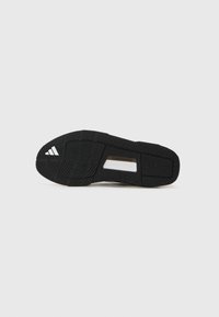 Sort sneaker sål med tekstureret gummi for greb. Har et mønster med tre striber og en hvid detalje med "TRAXION" branding.