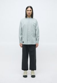 Lys grønn stripet oversized skjorte med høy krage og to sidelommer, kombinert med løse sorte bukser og beige sneakers.