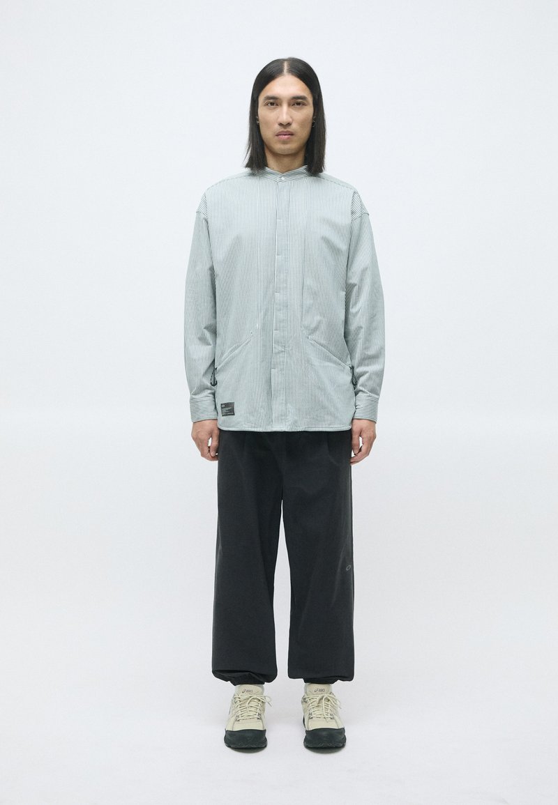 Lys grønn stripet oversized skjorte med høy krage og to sidelommer, kombinert med løse sorte bukser og beige sneakers.